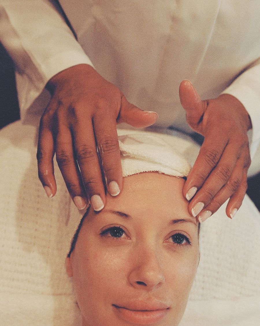 A therapist's hands resting gently on a client's forehead at the start of a facial treatment