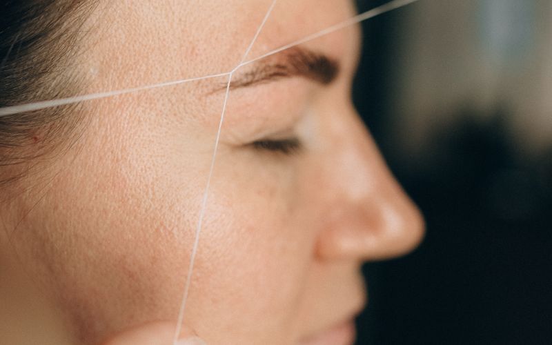A cotton thread being drawn across a client's brow during eyebrow threading